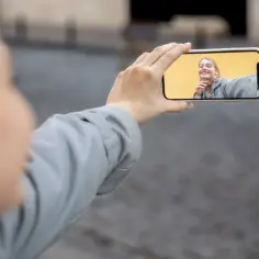 Kobieta trzyma telefon, by nagrać ekran z uśmiechniętą twarzą na żółtym tle.