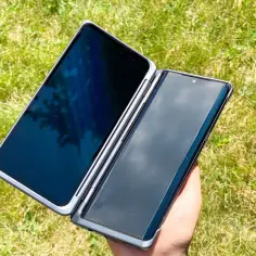 Dłoń trzyma otwarta obudowę LG Velvet Dual Screen na tle zielonej trawy.