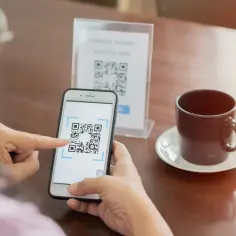 Osoba używa telefonu, by zeskanować kod QR ze zdjęcia. Widoczny jest ekran smartfona z ramką do skanowania kodu.