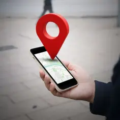 Dłoń trzyma smartfon z mapą, a nad nim unosi się czerwona pinezka. W ten sposób łatwo dowiedzieć się, jak wysłać pinezkę.