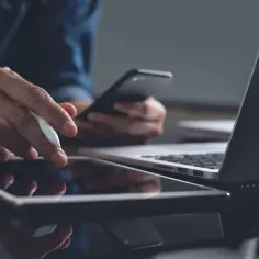 Mężczyzna pracuje na tablecie za pomocą rysika, trzymając telefon. Obok leży laptop. To jego codzienna sar.
