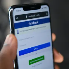 Dłoń trzyma smartfon z ekranem logowania Facebooka. Szukasz sposobu, jak odzyskać konto na FB bez maila i telefonu?
