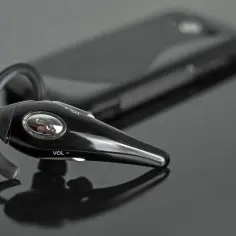 Czarna słuchawka Bluetooth leży obok telefonu. Idealna do tworzenia rankingu słuchawek bezprzewodowych.