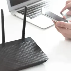 Router z antenkami, obok laptop i smartfon w dłoni, symbolizujące dostęp do sieci wlan.
