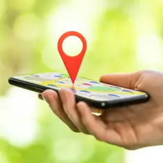 Dłoń trzyma smartfon z mapą i czerwoną pinezką wskazującą lokalizację telefonu.