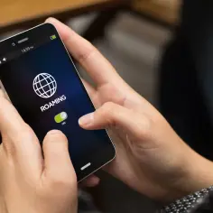 Dłoń włącza roaming na telefonie. Ikona globu i suwak "ON" wskazują, jak włączyć roaming.