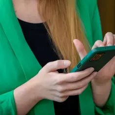 Kobieta w zielonej marynarce trzyma smartfon. Szuka informacji, gdzie jest schowek w telefonie Samsung, aby zabezpieczyć swoje dane.