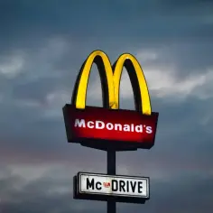 Podświetlany znak McDonald's z napisem "McDRIVE" na tle zachmurzonego nieba.