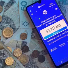 Smartfon z aplikacją do zarabiania na tle polskich banknotów i monet.