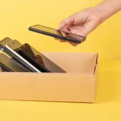 Ręka wkłada telefon do kartonu z innymi. Chcesz wiedzieć, jak sprawdzić jaki masz telefon?