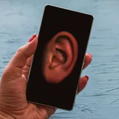 Dłoń trzyma smartfon z uchem na ekranie. Czy Twój telefon jest na podsłuchu?
