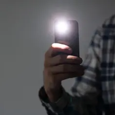 Dłoń trzyma smartfon z włączoną latarką.