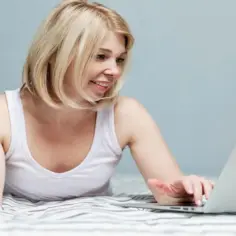 Kobieta z telefonem w ręku uczy się, jak udostępnić internet z laptopa, leżąc w łóżku.