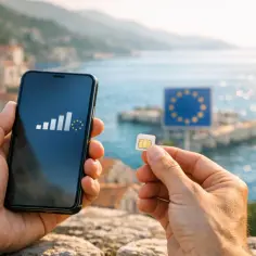 Ręce trzymają smartfon z ikoną zasięgu i symbolem UE oraz kartę SIM. W tle morze i znak UE. Nielimitowany internet w roamingu bez granic.