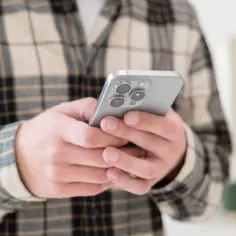 Dłonie trzymające telefon iPhone z widocznym modułem aparatów.