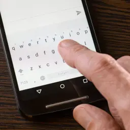 Palec naciska klawisz "Polski" na klawiaturze telefonu, pokazując, jak ustawić polskie znaki w SMS.