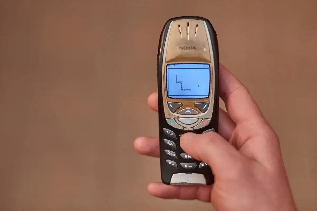 Dłoń trzyma starą Nokię, na której widać grę Snake. Klasyka telefonów komórkowych.