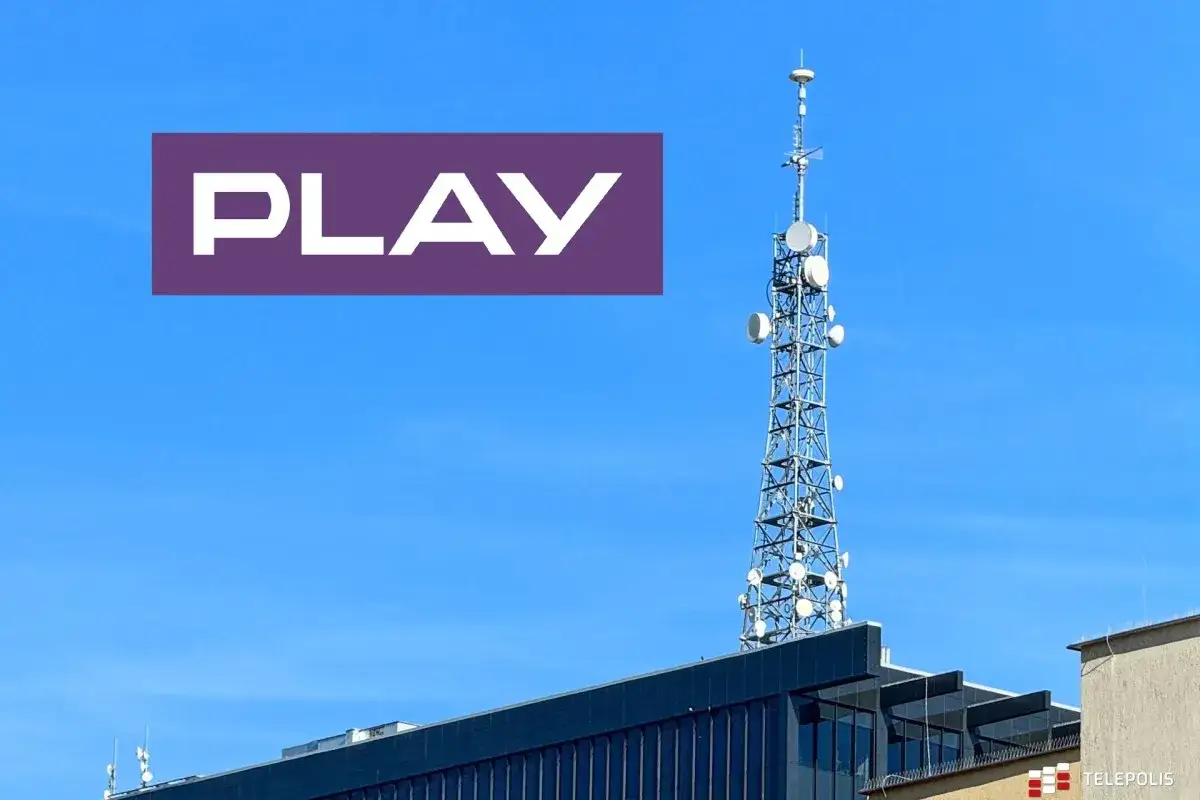 Maszt 5G Play na tle błękitnego nieba, z widocznym fragmentem budynku.