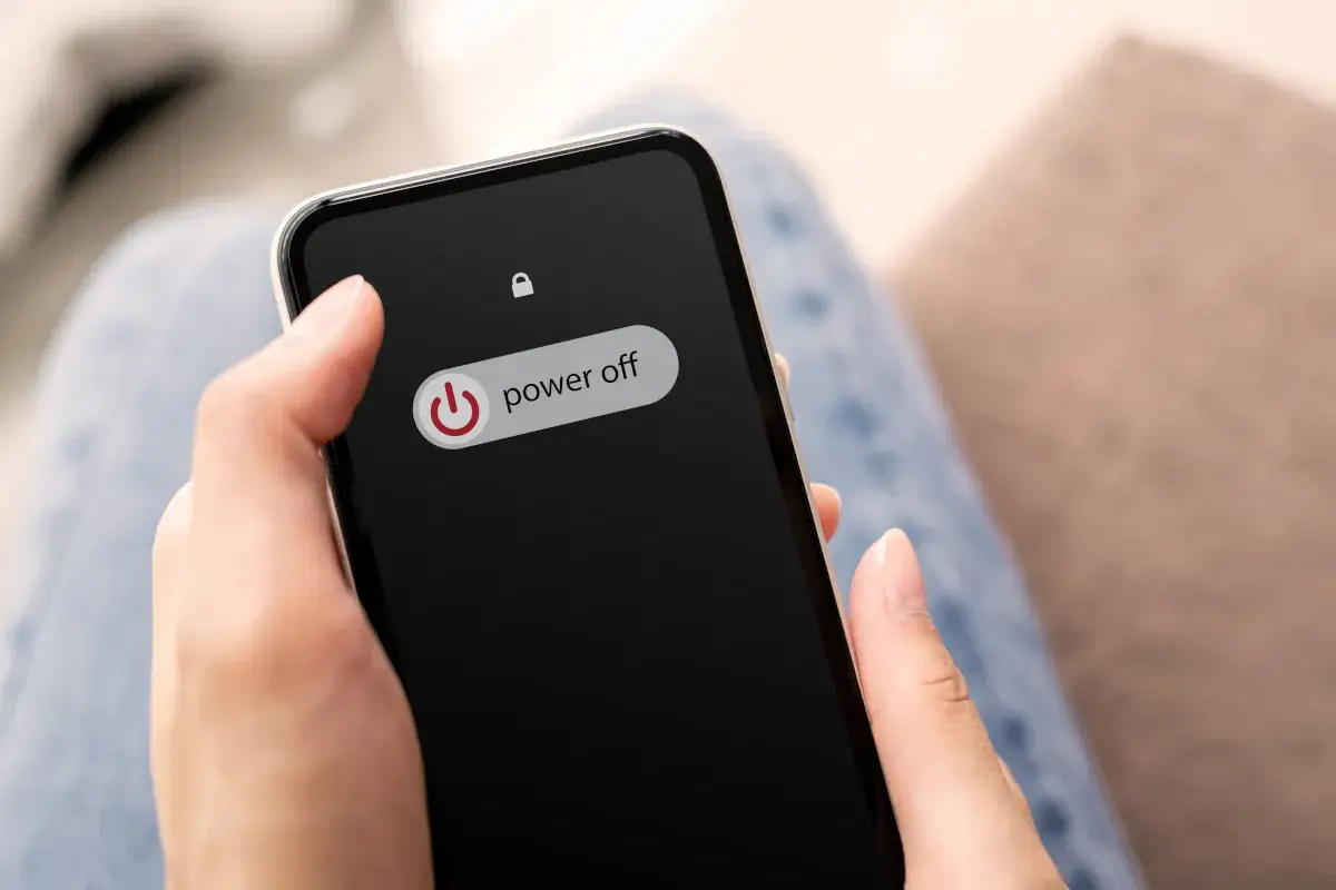 Dłoń trzyma smartfon z widocznym przyciskiem 