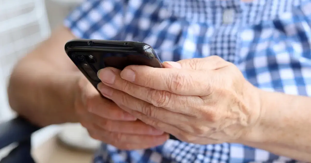 Dłonie starszej osoby trzymają smartfon. Może szuka informacji, jak namierzyć numer telefonu, lub korzysta z aplikacji.