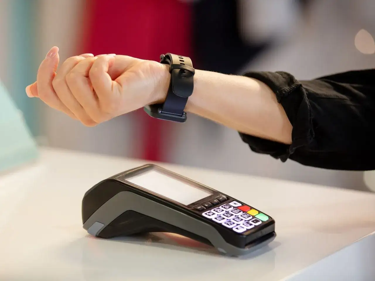 Dłoń z zegarkiem zbliża się do terminala płatniczego, by dokonać płatności zbliżeniowej za pomocą Garmin Pay.