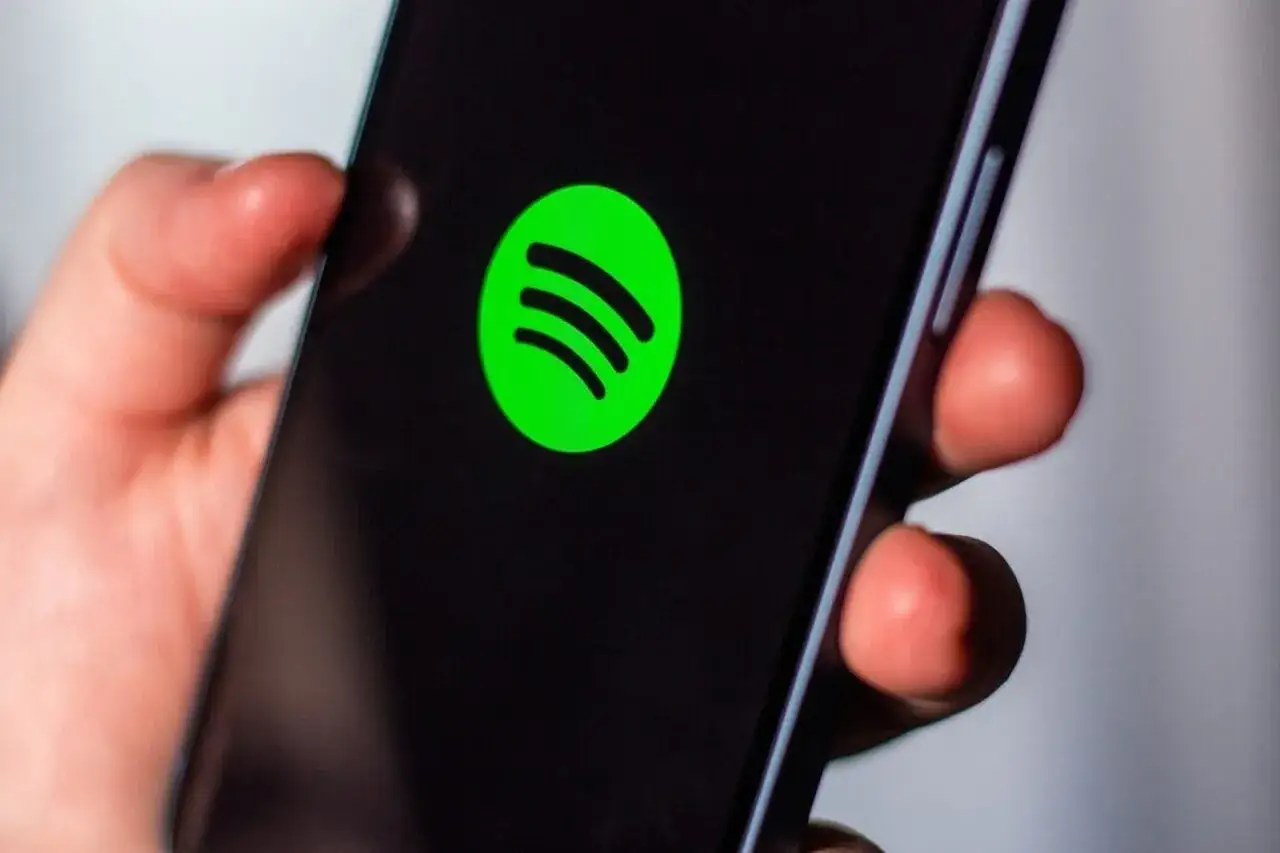 Dłoń trzyma smartfon z zielonym logo Spotify. Chcesz wiedzieć, jak zrezygnować z Spotify Premium?