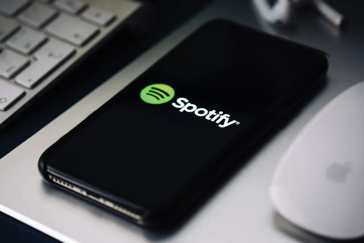 Telefon z logo Spotify na ekranie, obok klawiatura i myszka. Dowiedz się, jak zrezygnować z Spotify Premium.