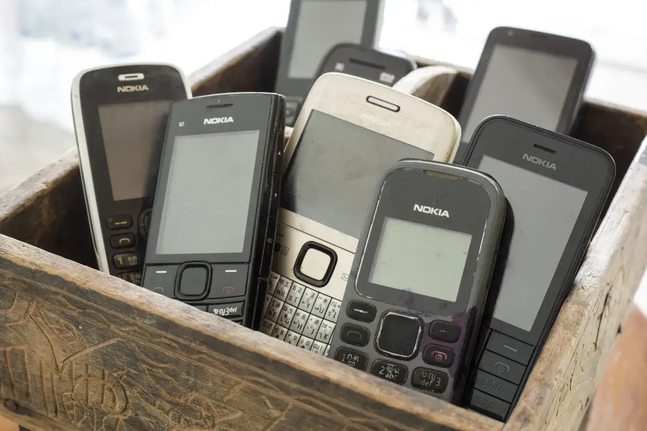 Kolekcja starych modeli Nokia w drewnianej skrzynce. Widać telefony z klawiaturami i ekranami, niektóre z nich noszą ślady użytkowania.