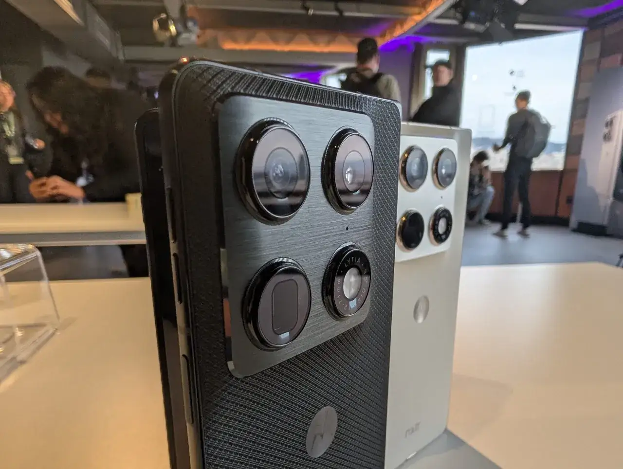 Dwa telefony Motorola Razr fold w zbliżeniu, jeden z czarnym, teksturowanym tyłem i modułem aparatów, drugi biały.