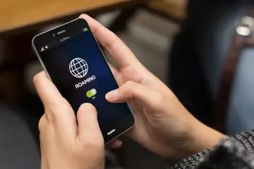 Dłoń włącza roaming na telefonie. Ikona globu i suwak "ON" wskazują, jak włączyć roaming.