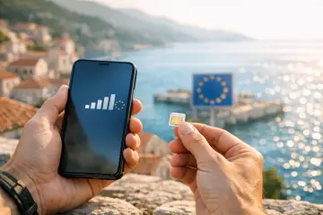 Ręce trzymają smartfon z ikoną zasięgu i symbolem UE oraz kartę SIM. W tle morze i znak UE. Nielimitowany internet w roamingu bez granic.